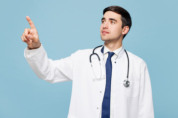 Young happy male doctor man wear white medical gown suit work in hospital clinic office touch something like push click on button isolated on plain blue background studio. Healthcare medicine concept