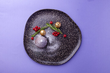 Festive dessert on dark speckled plate with rosemary, red berries and gold ornaments against purple.