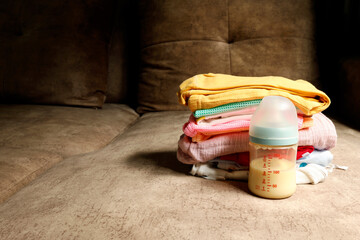 Baby milk bottle beside neatly folded baby clothes on a sofa, conveying warmth, childcare, and family lifestyle