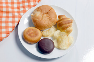 Assorted breads, pastries, and potato chips on a white plate, ideal for food, bakery, snack, and everyday lifestyle concepts