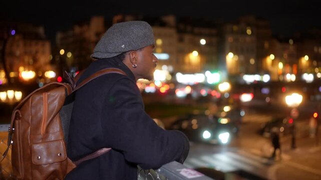Young man admiring paris city lights from a bridge at night