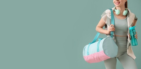 Young woman in sporty outfit, with bag, water bottle and headphones on mint background with space...