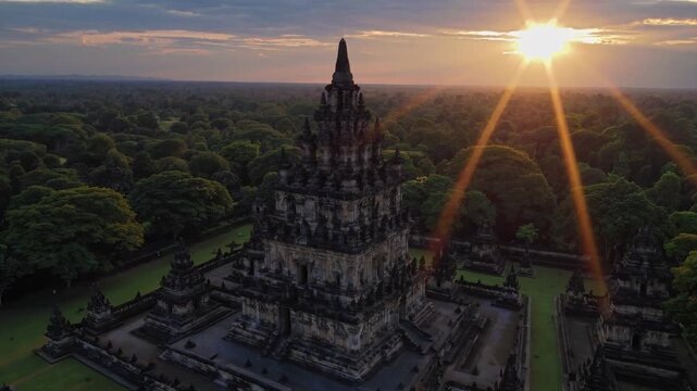 The majestic temple stands tall against the backdrop of a vibrant sunset, its intricate architecture silhouetted by the glowing sky. Surrounding lush trees enhance the beauty of th