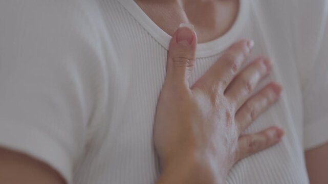 Close-up of a woman placing hand on her chest, indicating chest pain, heart discomfort, or emotional distress. Concept of heart attack symptoms, anxiety, or stress-related health issues.