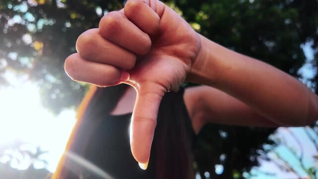 Close-up of a thumbs down hand gesture from low angle, front view, outdoors in nature. Concept of disapproval, rejection, negative feedback, failure, rating, evaluation, and nonverbal communication.