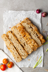 overhead view of slices of onion and scallion focaccia on parchment paper, top view of airy bubbly onion focaccia on a cement countertop