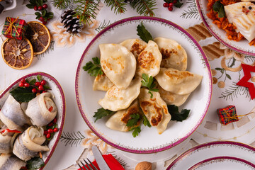Classic Christmas food medley on a decorated table. Fish, dumplings stuffed with cabbage and mushrooms, cheesecake, and ham.