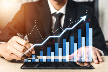 A business professional analyzes financial growth trends with a tablet and graphical data in a...