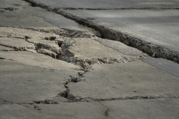 Damaged concrete road surface texture with deep cracks. Broken grey pavement background showing destruction, earthquake aftermath, and poor infrastructure condition.
