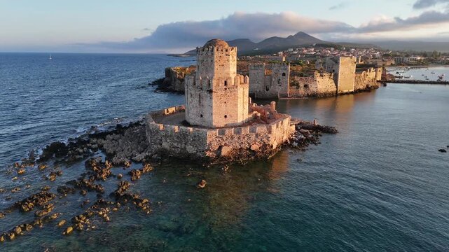 Methoni,Messenia,Peloponnese,Aerial view circular pan left around Bourtzi Tower during golden hour. Background are the Methoni Castle,the bay full with boats on anchor,beautiful landscape and clouds.