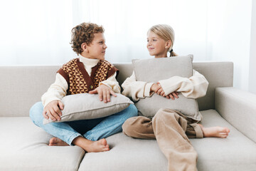 Authentic scene of children at home sharing a relaxed moment on a sofa with soft cushions, illustrating playful learning, friendship, and an everyday school lifestyle in a cozy setting.
