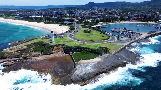 Drone aerial landscape of ocean waves crashing along coastline headland at Flagstaff Point Lighthouse with car driving past main road Wollongong Beach in Illawarra South Coast Australia travel tourism