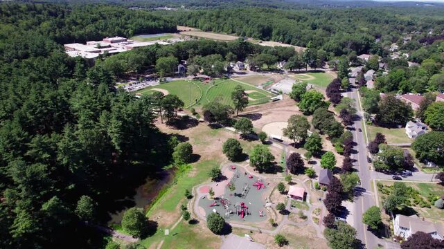 Wide aerial view of a recreational field area in Amesbury, Massachusetts. Three baseball diamonds, a skatepark and a playground are seen, with cars passing by along the border.