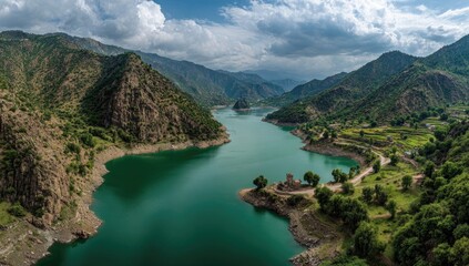 Panoramic view of a winding teal lake surrounded by lush green hills, under a cloudy sky