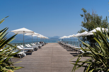 Lake Garda lakeside pier with sun loungers and white umbrellas on a sunny day