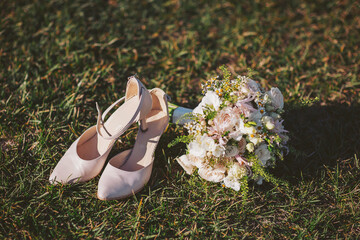 Wedding shoes and bouquet on green grass during afternoon light near a venue before the ceremony starts