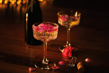 A beautifully detailed crystal glass filled with golden champagne and pink rose petals, bathed in soft, golden candlelight for an intimate and luxurious evening