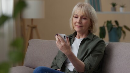 Old Caucasian woman looking in phone thinking at home relaxed 60s senior female retired lady using mobile app internet shopping decide think pensive with modern device cellphone dreaming pondering