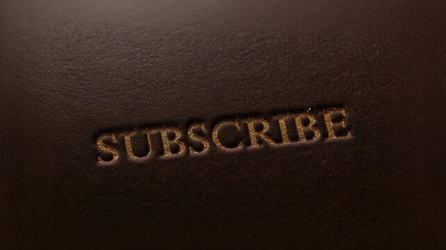 Shifting camera and sweeping warm light focusing on debossed SUBSCRIBE in dark brown leather studio