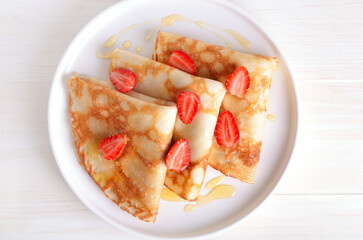 Homemade thin pancakes with strawberry slices and honey