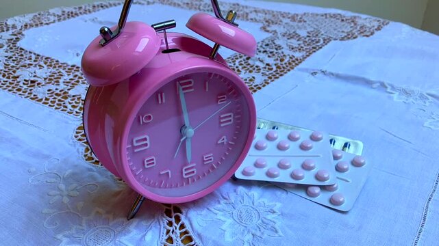 Pink alarm clock and pills on feminie bedside table 