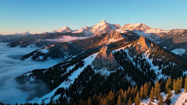 Majestic snowcapped alpine mountains rise above a sea of lowlying clouds during a breathtaking golden hour sunrise in the winter wilderness