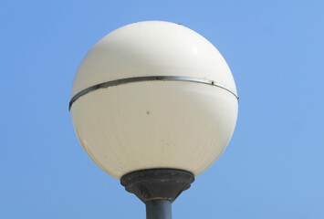 A tall white street lamp stands near an old metal water tower against a clear blue sky
