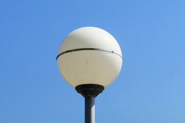 A tall white street lamp stands near an old metal water tower against a clear blue sky