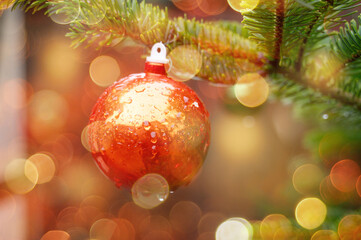 Red christmas bauble on a fir branch, bokeh fairy light, christmas market in rain, winter season