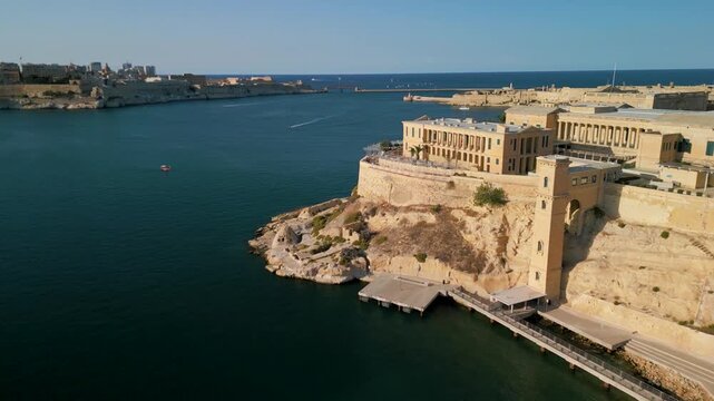 Aerial 4K 90-degree turn shot towards the historic Villa Bighi and Grand Harbour at sunset, Malta
