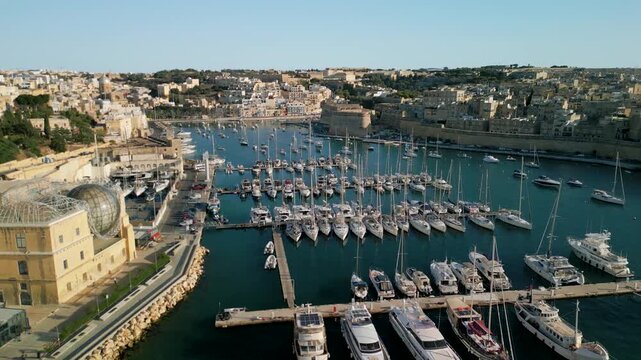 Aerial view of luxury yachts and sailboats in a crowded marina, Malta. Top down drone shot of turquoise Mediterranean water and summer nautical lifestyle.
