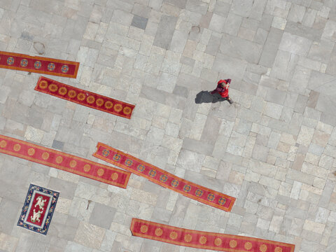 Aerial view of a person walking amidst vibrant red and patterned rugs spread across a stone courtyard, Thimphu, Bhutan.