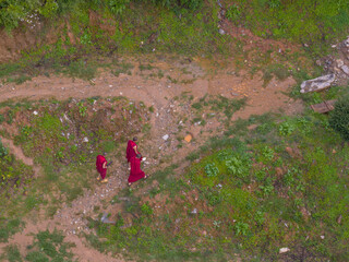 Aerial view of monks in deep red robes walking along a winding path, cutting through vibrant green slopes, the scene a blend of solemnity and natural beauty, Paro, Bhutan.