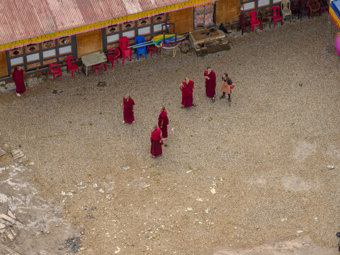 Aerial view of monks in red robes congregating in a sun-drenched courtyard, the scene rich with cultural texture and visual storytelling, Paro, Bhutan.