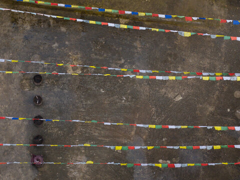 Aerial view of vibrant prayer flags strung tautly across a weathered surface, their colors a stark contrast against the muted tones, Paro, Bhutan.