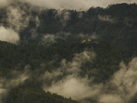 Aerial view of a monastery amidst the lush, emerald forest, shrouded in ethereal mist, where the architecture stands as a testament to Bhutanese heritage, Paro, Bhutan.