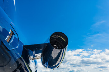 Rear view of the right turbofan engine on a small business jet. A bright blue sky fills the background, photographed close-up with fuselage in focus and clouds in soft focus.