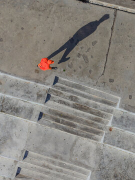 Aerial view of a solitary figure in vibrant orange casting a long shadow on weathered concrete steps, Thimphu, Bhutan.