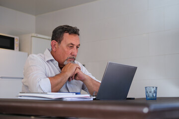 Mature man studying focused on laptop at home