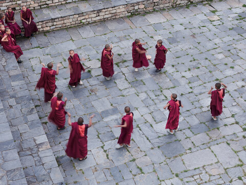 Karpo Lhakhang, Bhutan - 25 September 2025: Aerial view of monks in vibrant maroon robes dancing on the cool, grey stone courtyard, framed by tiered steps.