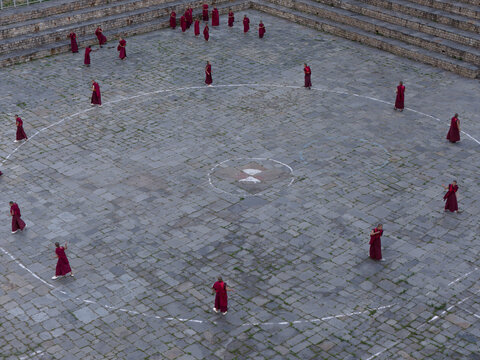 Karpo Lhakhang, Bhutan - 25 September 2025: Aerial view of monks in maroon robes standing in a circle on the grey stone ground, a dance of faith and tradition unfolds.