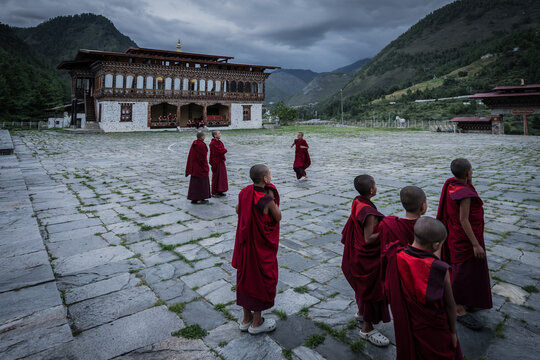 Haa, Bhutan - 25 September 2025: View of crimson-robed monks wander across the stone courtyard of Lhakhang Karpo monastery, nestled against the dramatic backdrop of hazy mountains.