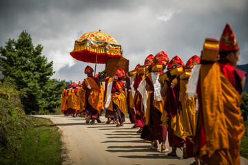 Nubding, Bhutan - 21 September 2025: View of monks in vibrant saffron robes, process along a winding road in Phobjikha Valley under a decorative parasol.