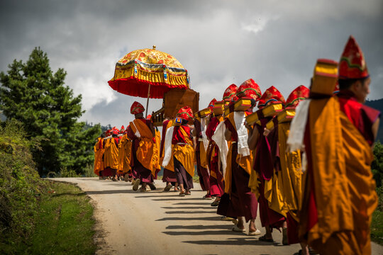 Nubding, Bhutan - 21 September 2025: View of monks in vibrant saffron robes, process along a winding road in Phobjikha Valley under a decorative parasol.