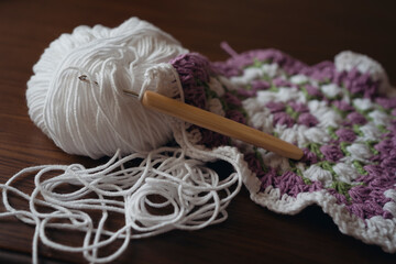 Crochet hook and ball of white yarn and unfinished square napkin
