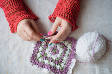 female hands crocheting colorful square napkin of multicolor yarn