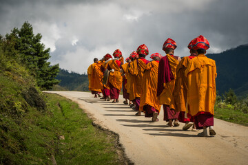 Nubding, Bhutan - 21 September 2025: View of monks in vibrant saffron robes walking along a winding road in Phobjikha Valley, against a backdrop of rolling hills and a dramatic, cloudy sky.