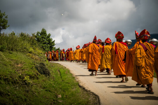 Nubding, Bhutan - 21 September 2025: View of a procession of monks in vibrant orange robes winds along a path in Phobjikha Valley, under a sky heavy with dramatic clouds.
