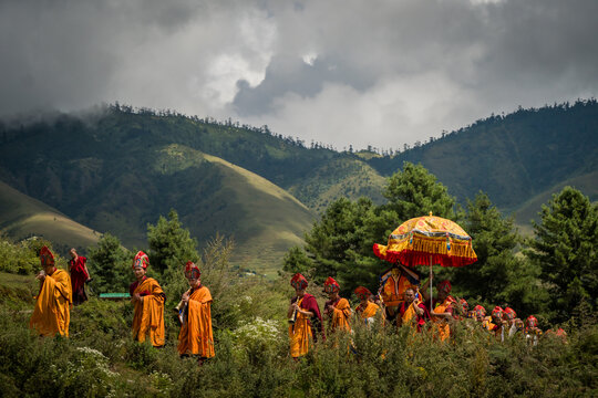 Nubding, Bhutan - 21 September 2025: View of monks in vibrant orange robes processing through the Phobjikha Valley, under a decorative parasol, against a backdrop of misty mountains.