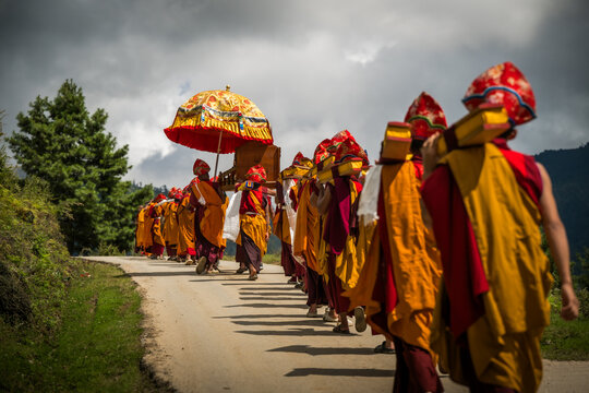 Nubding, Bhutan - 21 September 2025: View of monks in vibrant saffron robes and ornate hats walking along a winding road in Phobjikha Valley, carrying a golden umbrella.